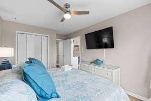 A bedroom with a bed, a ceiling fan, a TV, a dresser, and a door leading to another room. - Infinity Dream𓇼Ocean Views+Sleeps 14+Golf Cart (Oak Island)