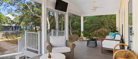 A covered outdoor area with seating, a television, and a ceiling fan.
