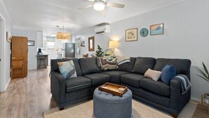 A modern living room with a sectional sofa, a coffee table, and a ceiling fan. - Birdsong Cottage𓇼Island Retreat+Central Location (Oak Island)