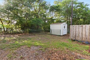 A fenced backyard with a shed, trees, and a wooden fence. - Birdsong Cottage𓇼Island Retreat+Central Location (Oak Island)