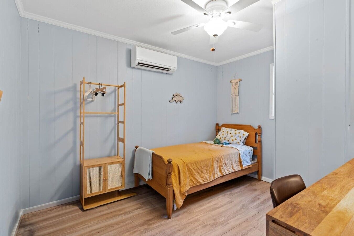 A bedroom with a single bed, a wooden wardrobe, a ceiling fan, and an air conditioning unit.