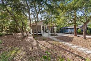 A house with a porch, surrounded by trees and a gravel driveway. - Birdsong Cottage𓇼Island Retreat+Central Location (Oak Island)