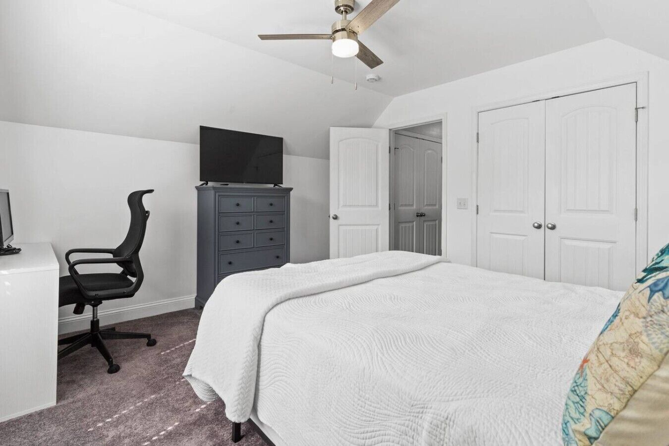 A bedroom with a bed, a desk with a chair, a dresser, and a ceiling fan.