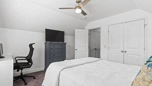 Ein Schlafzimmer mit einem Bett, einem Schreibtisch mit Stuhl, einer Kommode und einem Deckenventilator.