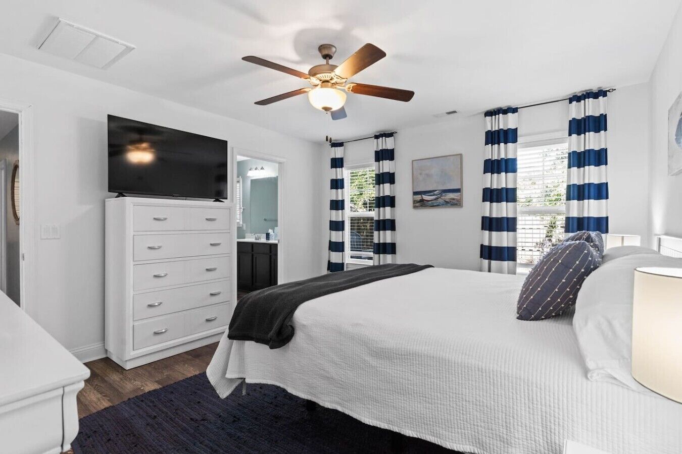 A bedroom with a bed, a dresser, a television, and a ceiling fan.