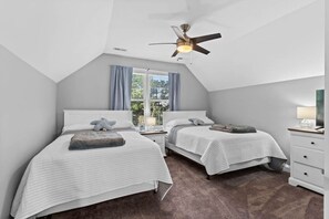 Ein Schlafzimmer mit zwei Betten, einem Deckenventilator, einem Fenster mit Vorhängen und einem Nachttisch mit Lampe.