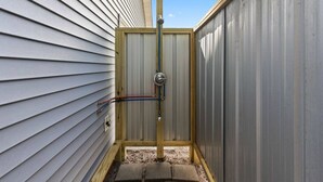Ein kleiner, umzäunter Außenbereich mit einer Metalttür, Holzrahmen und sichtbarer Elektroverkabelung.