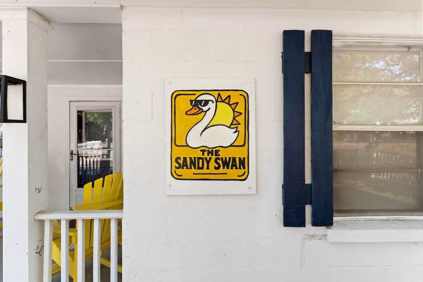 A building with a sign that reads 'The Sandy Swan' and a yellow chair outside.