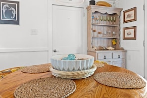 Una mesa de comedor con individuales tejidos, un cuenco decorativo y un aparador de madera con cristalería.