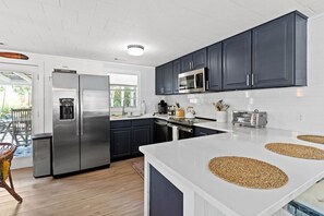 A modern kitchen with dark cabinets, stainless steel appliances, and a white countertop. - Sandy Swan𓇼Cozy Cottage Vibes+Golf Cart+Hot Tub (Oak Island)