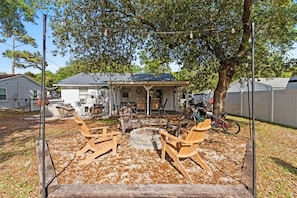 A backyard with a fire pit, wooden chairs, and a covered patio area. - Sandy Swan𓇼Cozy Cottage Vibes+Golf Cart+Hot Tub (Oak Island)