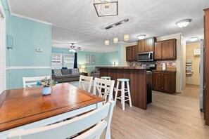 A kitchen with wooden cabinets, a microwave, and a dining area with a wooden table and white chairs.