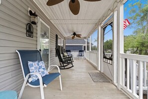 A covered porch with a ceiling fan, two rocking chairs, and a bench.