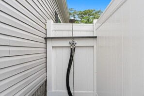A white exterior wall with horizontal siding and a black hose attached to a white fence.