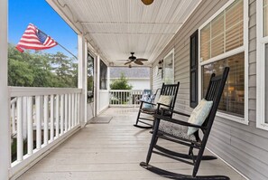 A covered porch with two rocking chairs, a ceiling fan, and a view of the house.