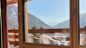 Una stanza con un divano, un tavolino in vetro, una panca in legno e vista sulle montagne attraverso ampie finestre.