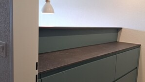 Una cucina con un piano di lavoro verde scuro, una lampada a sospensione bianca e un soffitto bianco.