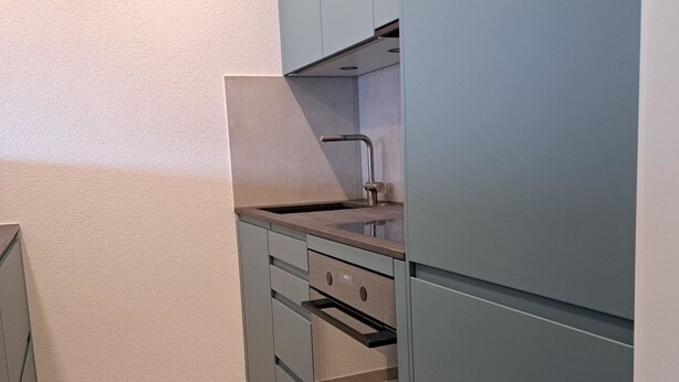 Una cucina compatta con forno integrato, lavello e pensili.