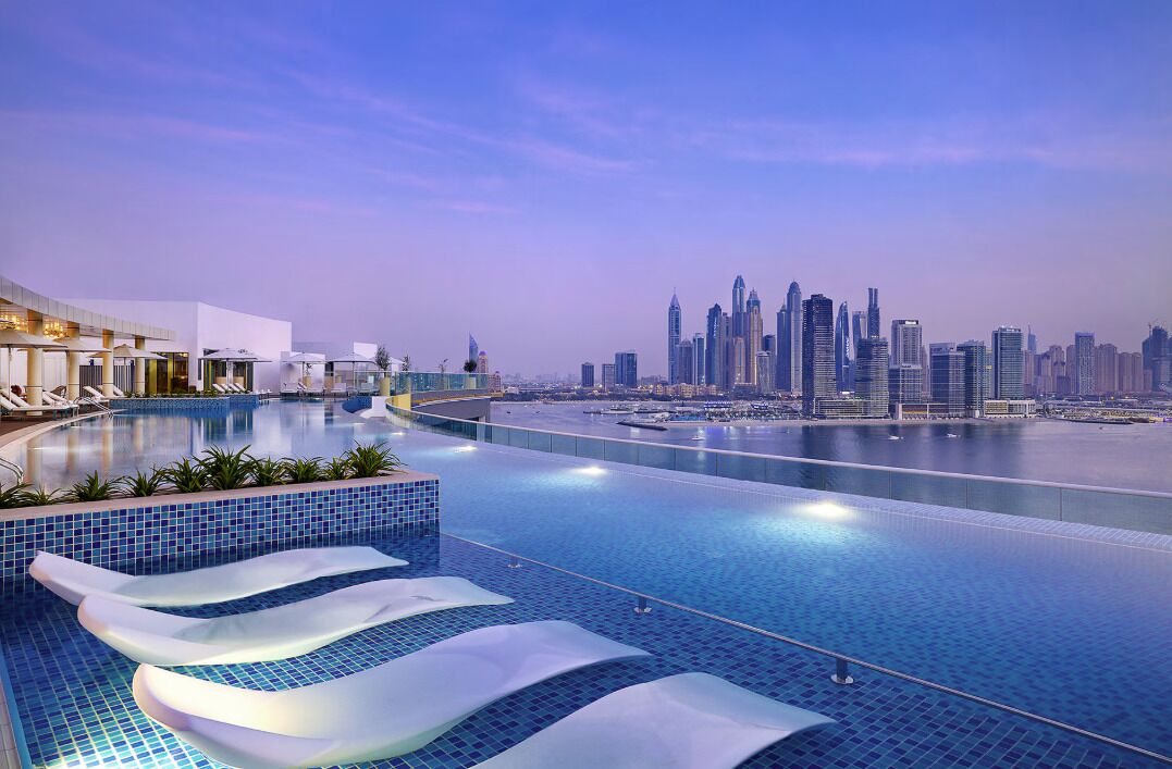 Une piscine moderne d’hôtel offrant une vue sur les gratte-ciel de la ville, avec des chaises longues et un ciel dégagé.