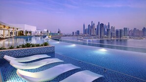 Ein moderner Pool eines Hotels mit Blick auf die Stadtlandschaft, Liegestühle und einem klaren Himmel.