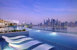 Ein moderner Pool eines Hotels mit Blick auf die Stadtlandschaft, Liegestühle und einem klaren Himmel.