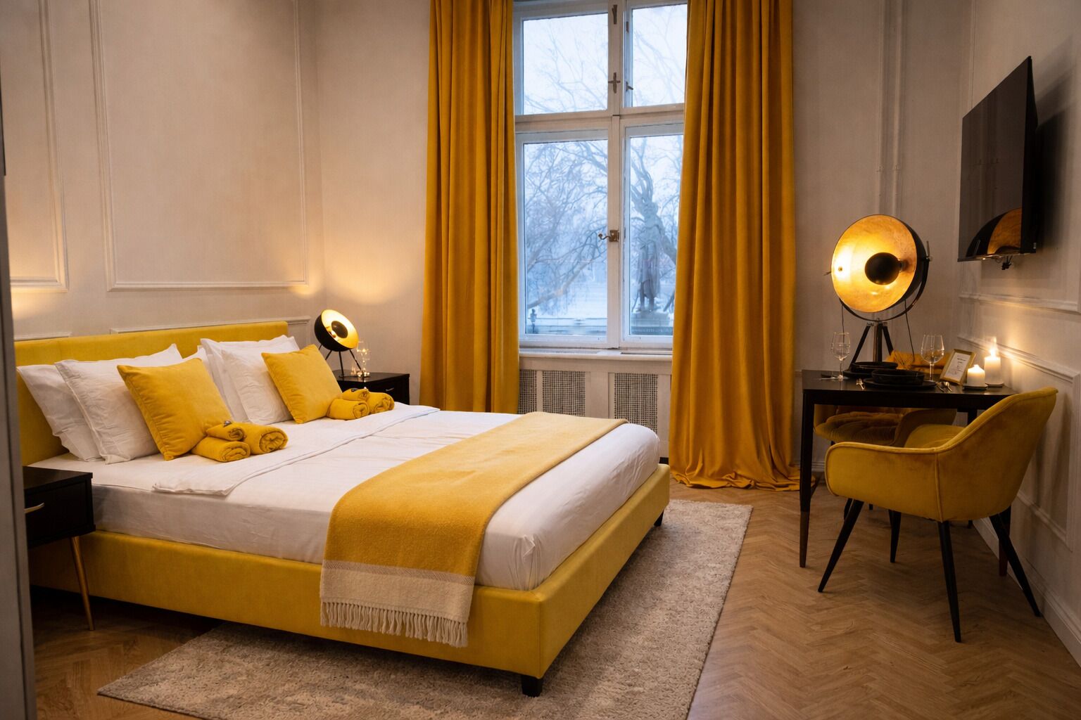 Habitación de hotel con cama, escritorio, silla, lámpara y ventana con cortinas.