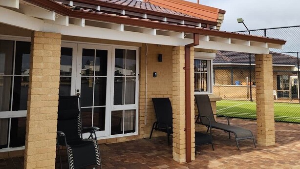 Ein überdachter Patio-Bereich mit Backsteinböden und zwei schwarzen Stühlen.