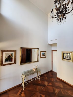 A hallway with a wooden parquet floor, a glass console table with a vase, and three framed pictures on the wall. - Mandurah Holiday Apartments ‘Pelican’ (Dudley Park)