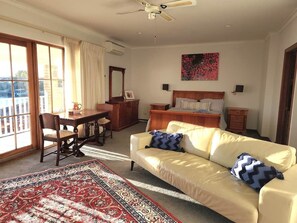 A room with a bed, a sofa, a desk, and a chair. There is a window with curtains and a view outside. - Mandurah Holiday Apartments ‘Osprey’ (City of Mandurah)