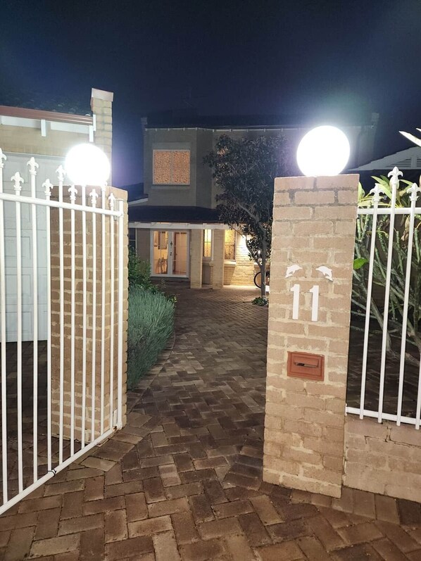 Une entrée fermée par un portail mène à un immeuble, et un chemin pavé de briques conduit à l’entrée.