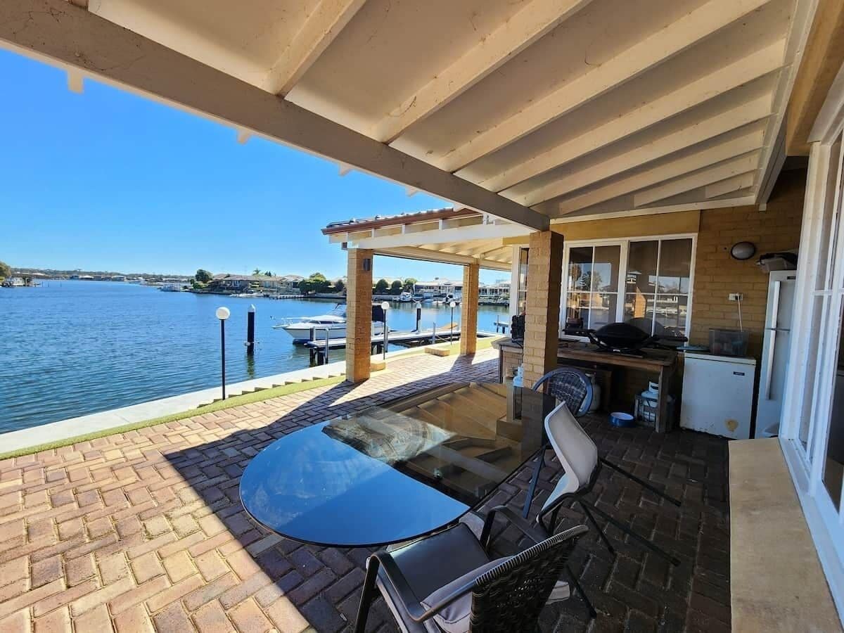 En overdækket terrasse med bord og stole, der vender ud mod et vandareal.