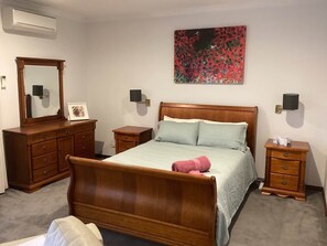 Une chambre à coucher avec un lit en bois, une commode, une table de chevet et un tableau accroché au mur.