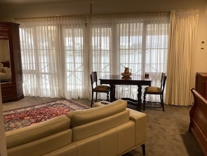 Una sala de estar con sofá, una mesa de comedor con sillas, un tapete y cortinas translúcidas.