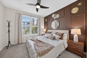 Ein Schlafzimmer mit Bett, Nachttischlampen, Deckenventilator, Kleiderständer und einem Fenster mit Jalousien.