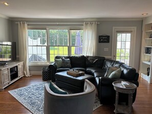 Ein Wohnzimmer mit einer Ledersofa, einem Fernseher auf einem Schrank und einem Bücherregal.