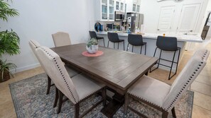 Een eetruimte met een houten tafel, vier stoelen, een kleine potplant en een keuken op de achtergrond.