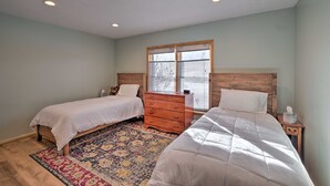 A bedroom with two beds, a wooden dresser, a patterned rug, and a window with blinds.