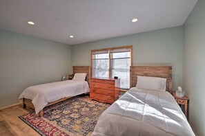 A bedroom with two beds, a wooden dresser, a patterned rug, and a window with blinds.