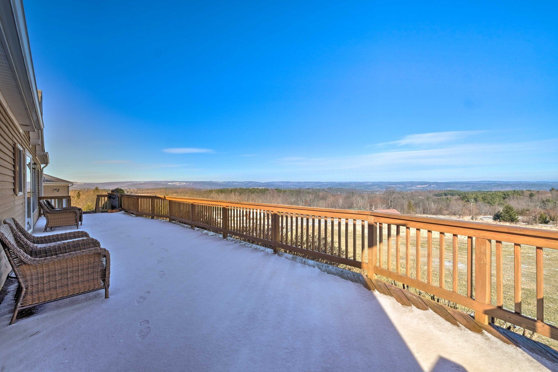 A snow-covered deck with wicker furniture and a view of distant hills.