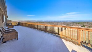 A snow-covered deck with wicker furniture and a view of distant hills.