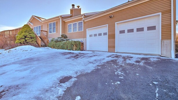 A residential property with a garage, a staircase, and a snow-covered driveway.