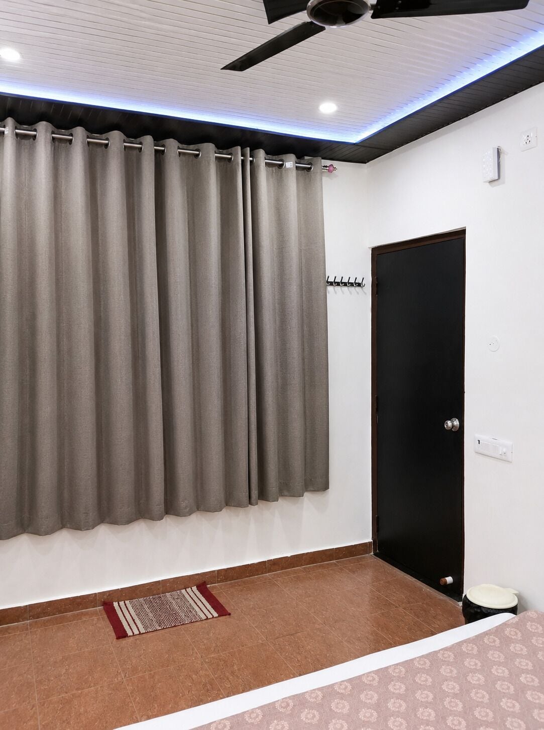 Una habitación con ventilador de techo, una puerta negra y un tapete estampado.
