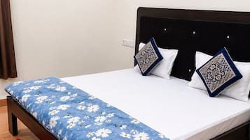 A bed with a blue floral bedspread, two patterned pillows, a red rug, and a wall-mounted air conditioner.
