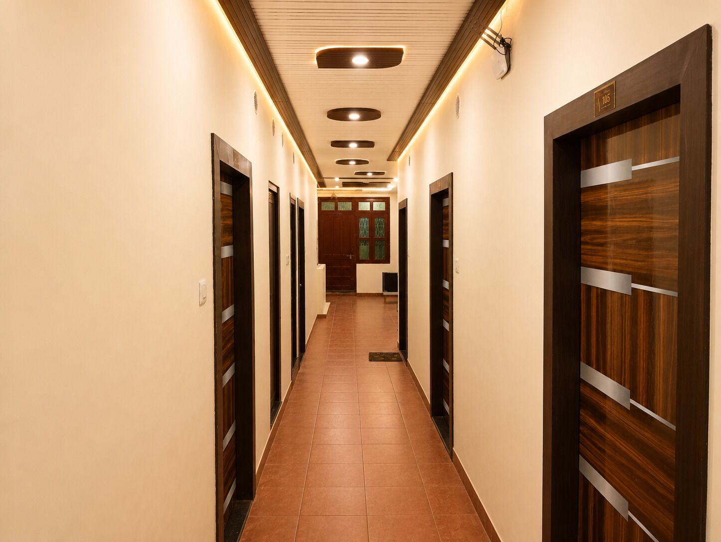 Een hotelgang met meerdere deuren, een betegelde vloer en een plafond met inbouwverlichting.