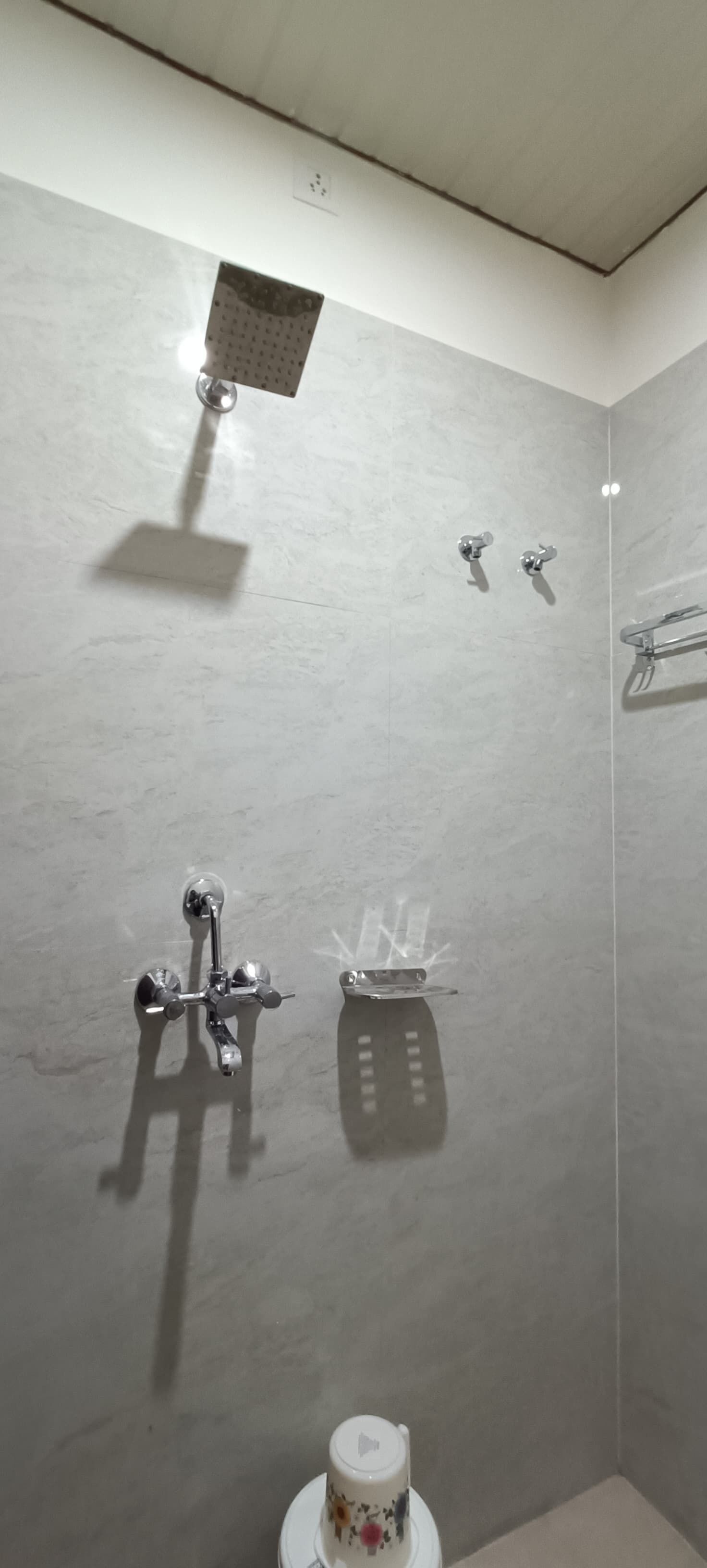 A shower area with a handheld showerhead, a wall-mounted faucet, and a towel rack.