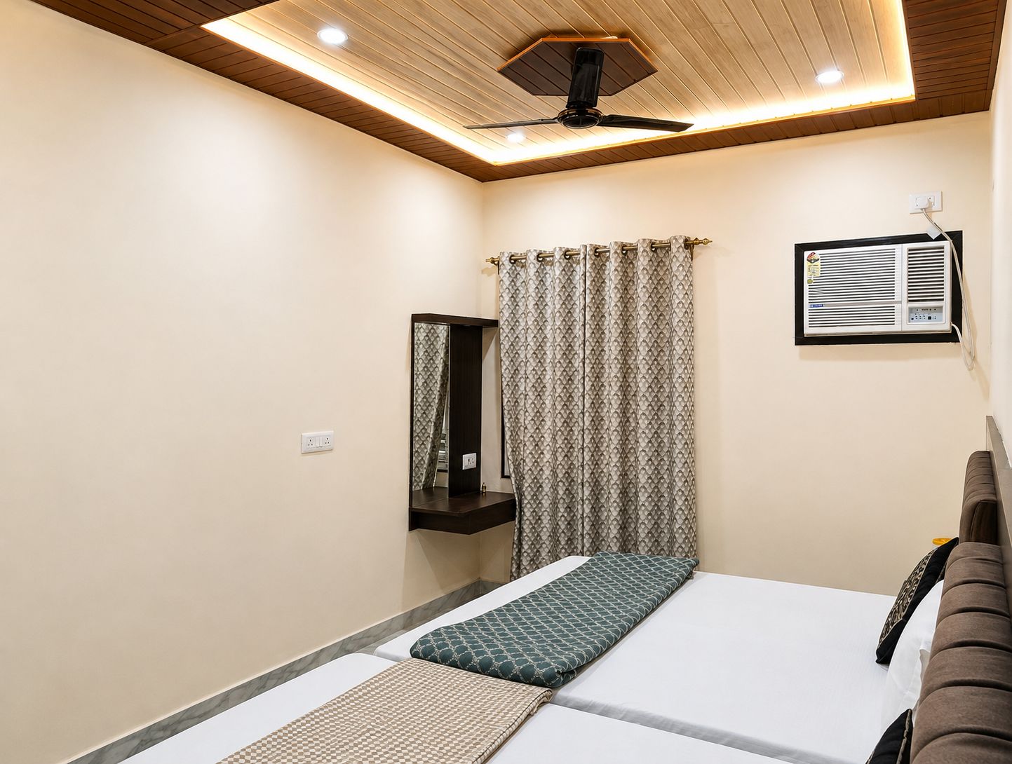 A bedroom with a bed, a ceiling fan, a window with curtains, a wall-mounted air conditioner, and a mirror.