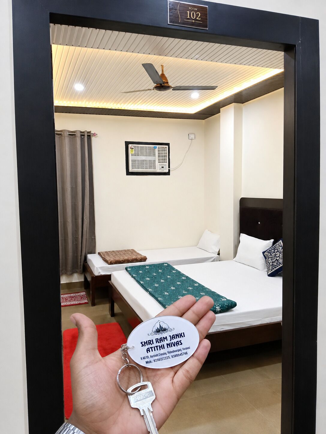 A hotel room with a bed, a ceiling fan, an air conditioning unit, and a sign indicating the room number.