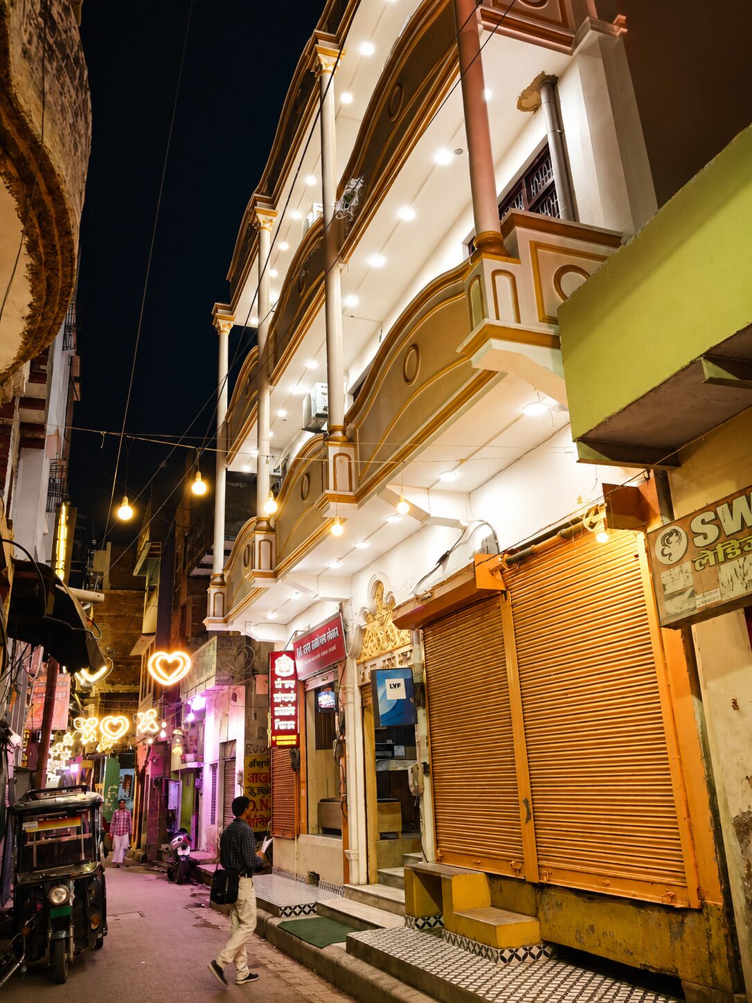 Una calle estrecha con edificios que presentan fachadas ornamentadas y letreros iluminados, lo que sugiere un área histórica o de importancia cultural.