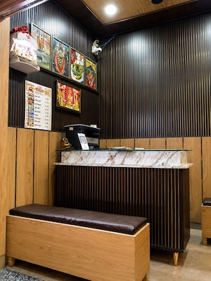 A restaurant interior with a wooden bench, a counter with a menu, and decorative wall art. - Shri Ram Janki Atithi Nivas (Varanasi)
