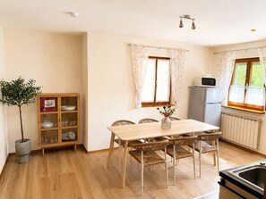 A compact kitchen with a dining table, chairs, a cabinet, a refrigerator, and a potted plant.